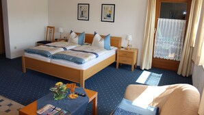 A hotel room with a large bed, bedside tables, a desk with a chair, and a window with curtains.