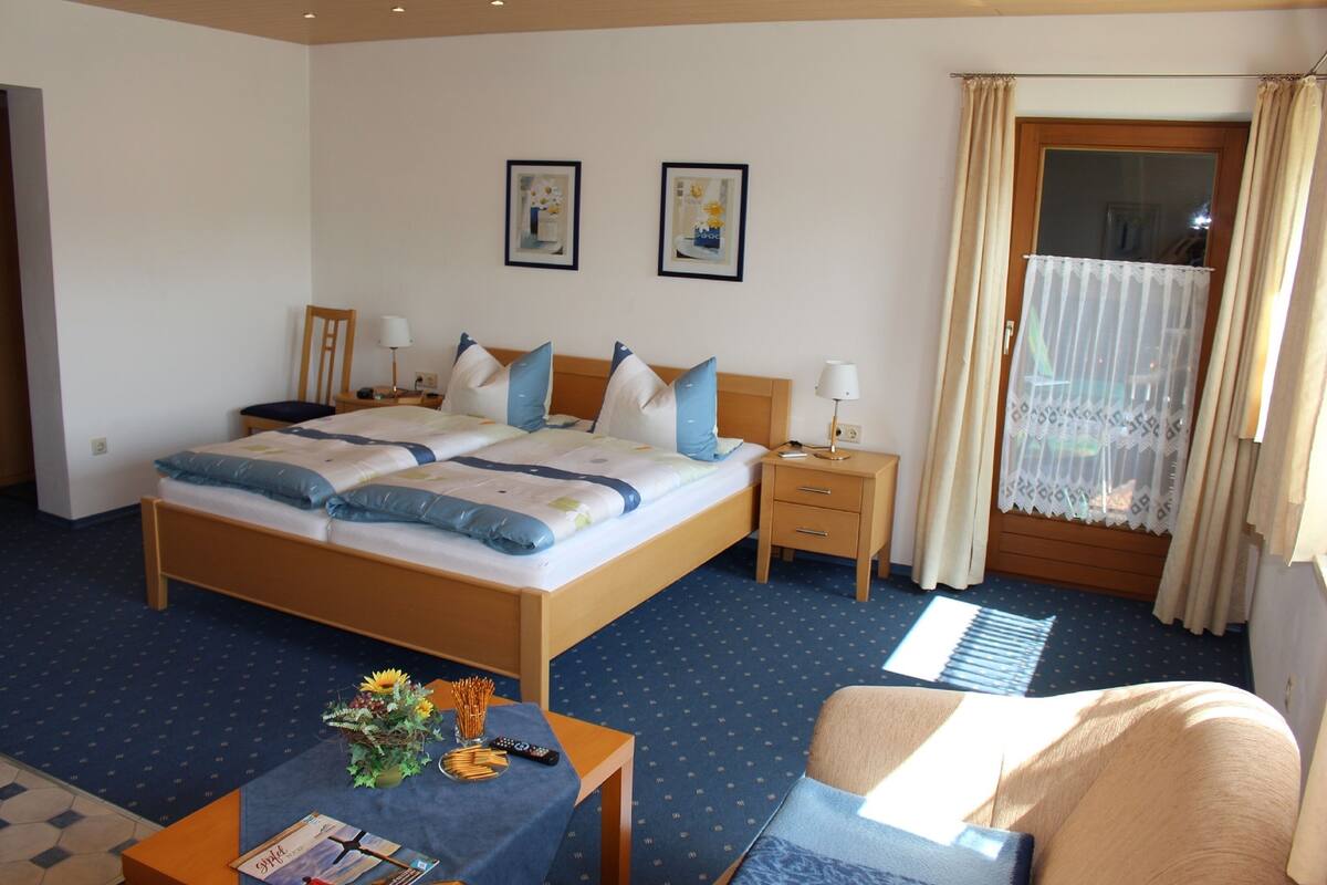 A hotel room with a large bed, bedside tables, a desk with a chair, and a window with curtains.