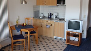 A compact kitchen with wooden cabinets, a microwave, a coffee maker, and a television on a stand.