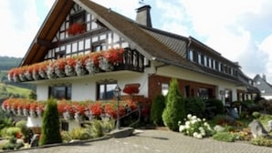 Una cabaña tradicional con techo pronunciado, ventanas dormer y un balcón decorado con flores rojas.