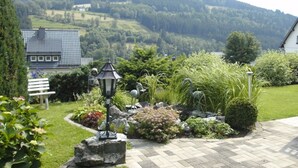 A garden with a bench, a lamp post, and a view of a house and hills in the background. - Pension Sonnenblick (Winterberg)