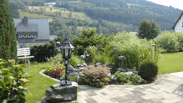 Un jardín con un banco, una farola y vistas a una casa y colinas al fondo.