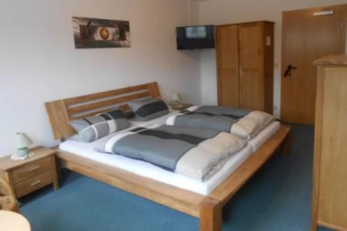 A bedroom with a wooden bed, a nightstand, a television, and a wardrobe.
