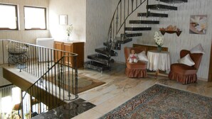 Amplia sala de estar con piso de mármol, una escalera, un comedor con mesa y sillas, y un tapete decorativo.