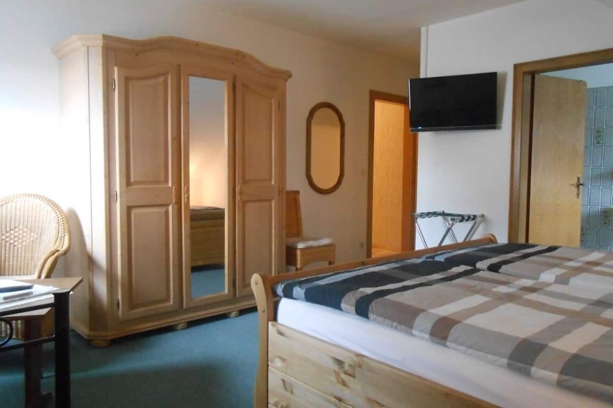A bedroom with a bed, wardrobe, chair, and a television on the wall.