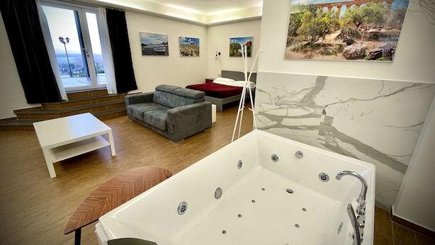 A modern living room with a sofa, a small table, a large bathtub, and a balcony with a view.