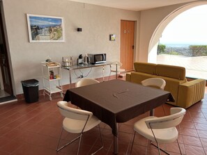 A dining area with a table, chairs, a sofa, a trash bin, a coffee station, and a view through an arched window. - Villa Leucatia Bed&Events (Sant'Agata Li Battiati)