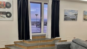 A living room with a grey sofa, a staircase leading to a balcony, and artwork on the walls.