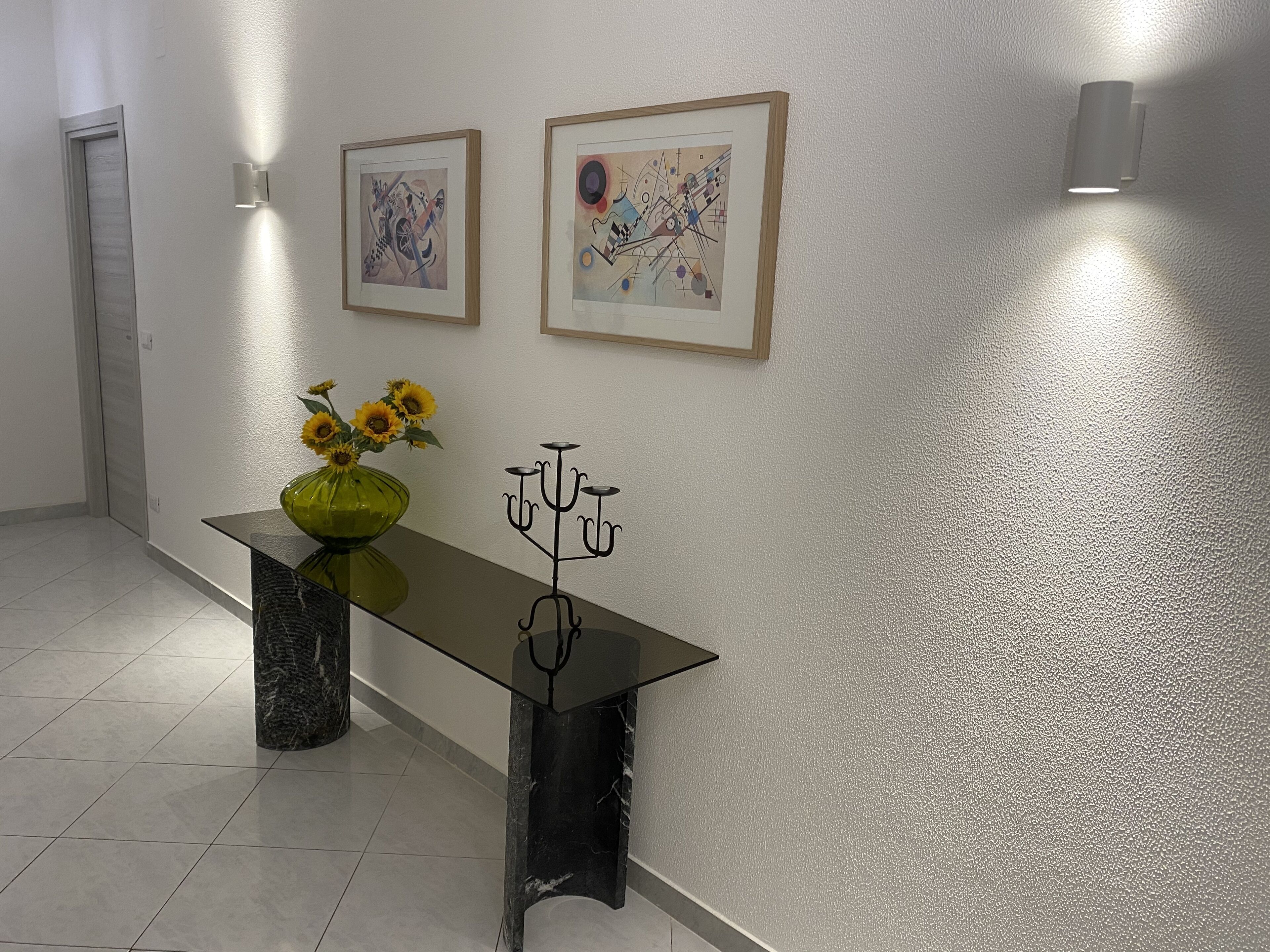 Ein Korridor mit einem Marmortisch, einer Vase mit Sonnenblumen, zwei gerahmten abstrakten Gemälden und einer Wandleuchte.