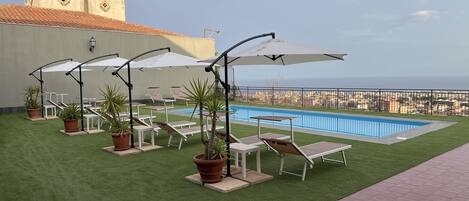 Een buitenzwembad, parasols bij het zwembad en ligstoelen