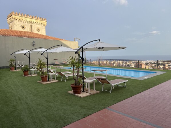 A rooftop pool area with lounge chairs and umbrellas, a pool, and a view of a cityscape and tower in the background. - Villa Leucatia Bed&Events (Sant'Agata Li Battiati)
