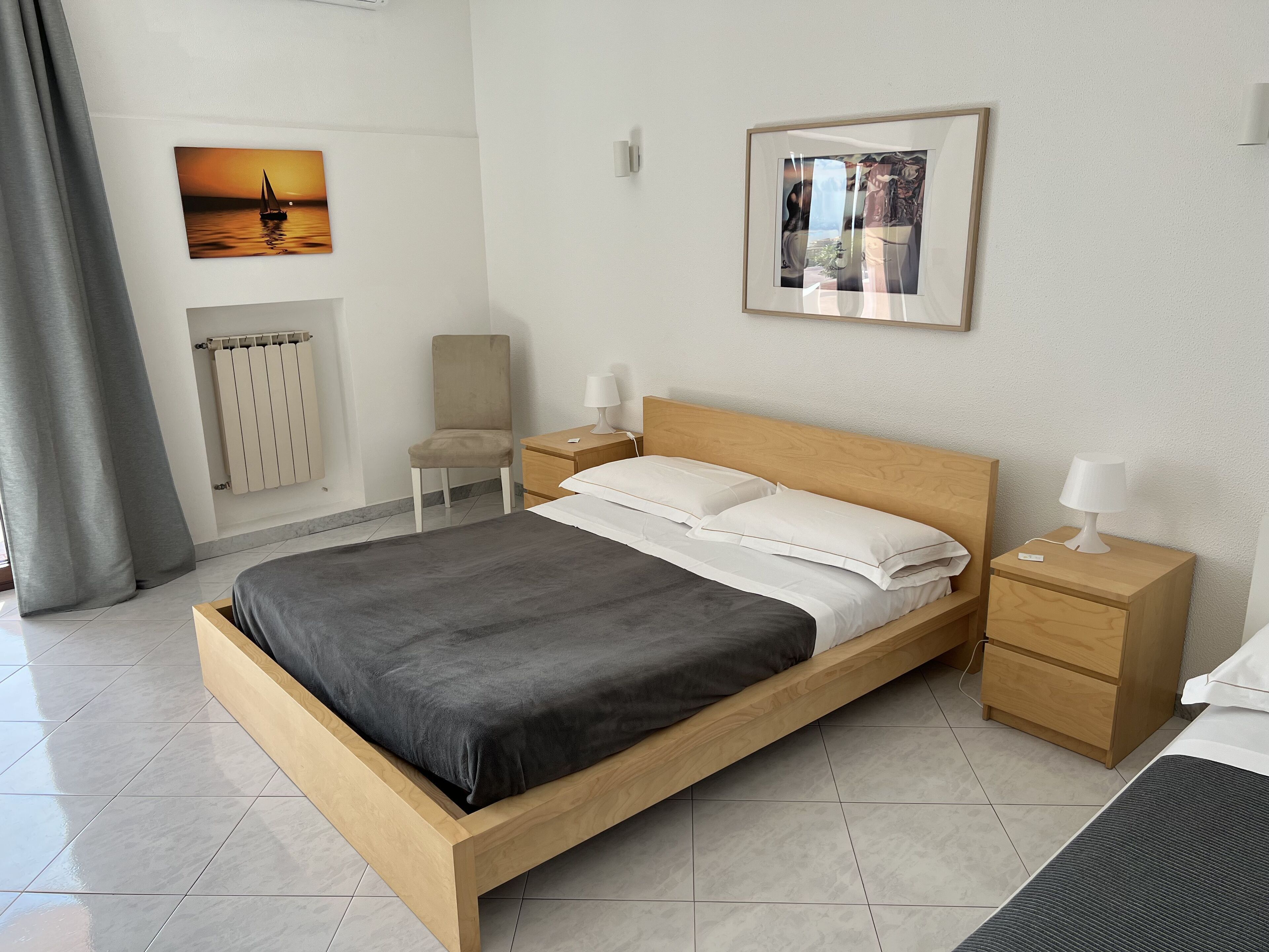 Ein ordentlich eingerichtetes Schlafzimmer mit einem hölzernen Bett, Nachttischen, einem Sessel und zwei gerahmten Bildern an den Wänden.