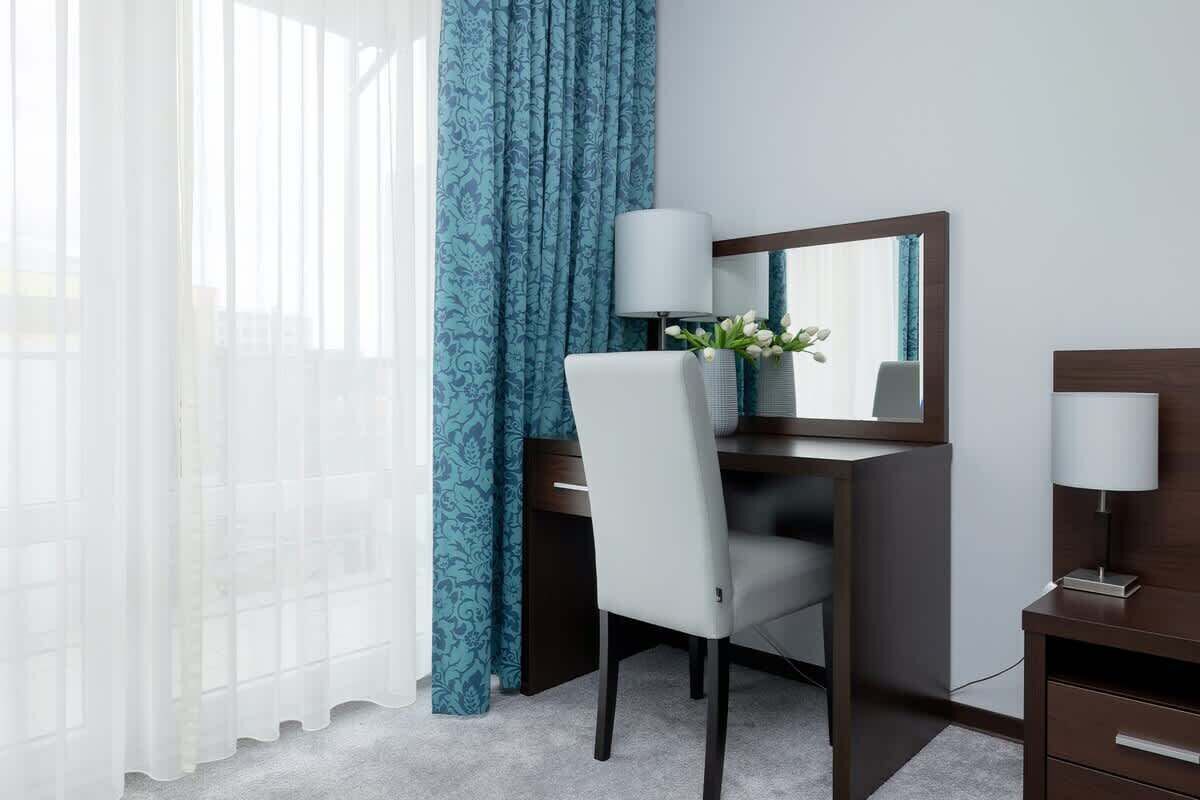 A hotel room with a desk, chair, and a mirror.