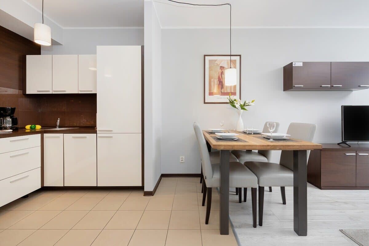 A modern kitchen with white cabinets, a dining table with chairs, a TV, and a framed picture on the wall.