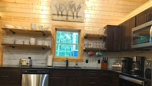 Una cucina con pareti in legno, una finestra vista alberi, elettrodomestici in acciaio inossidabile e mobili in legno.