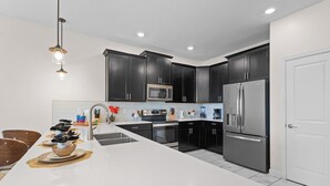 Une cuisine moderne avec des meubles de couleur sombre, des appareils en acier inoxydable et un îlot central blanc.