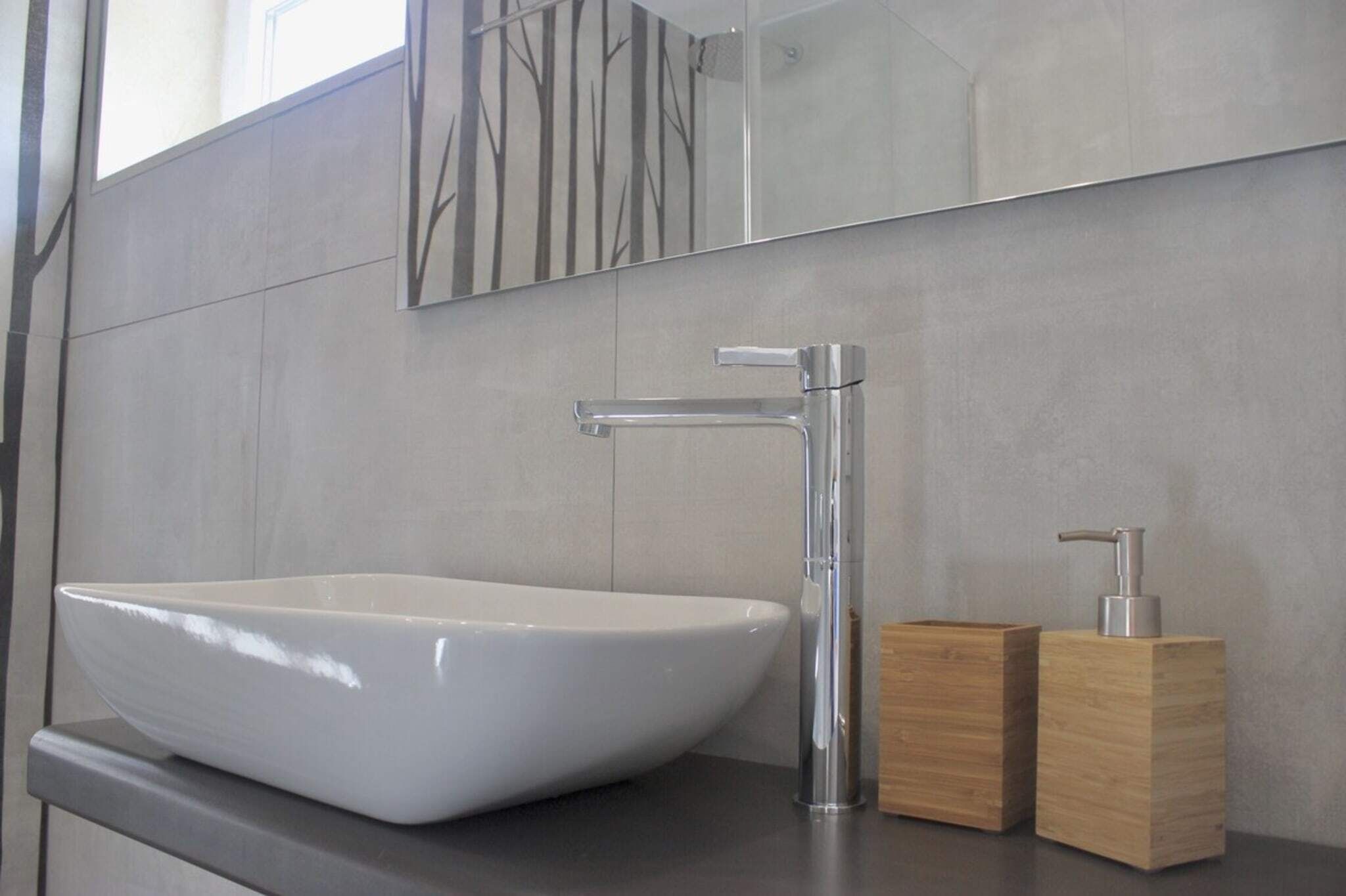 A modern bathroom with a white vessel sink, a chrome faucet, and wooden soap dispensers.