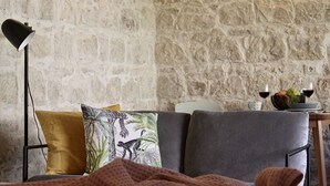 A cozy living room with a stone wall, a sofa with cushions, a floor lamp, and a small table with a bowl of fruit and glasses. - Cottage Myrtle (Giarratana)