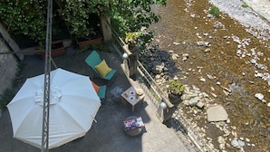 An outdoor patio area with a white umbrella, a round table with a colorful cushion, and a small table with a plate and glass. - Bridge Apartment Argegno (Argegno)