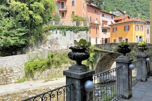 A stone bridge with a railing, a river below, and buildings with balconies in the background. - Bridge Apartment Argegno (Argegno)