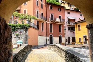 A courtyard with stone walls, a stone floor, and buildings with balconies and windows. - Bridge Apartment Argegno (Argegno)