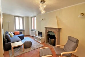 A living room with a fireplace, a sofa, a television, and a chair. - Bridge Apartment Argegno (Argegno)