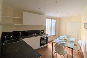 Eine kleine Küche mit Herd, Backofen und Spüle, einem Esstisch mit Stühlen und einem Fenster mit Vorhängen.