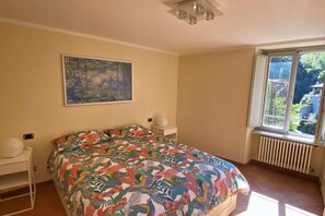 Ein Schlafzimmer mit einem großen Bett, einem Fenster mit Blick auf Grünflächen, einem Bild an der Wand und einem Heizkörper unter dem Fenster.