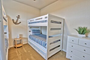 Een stapelbed met streepjesbeddengoed, een klein houten krukje, een witte dressoir en een decoratieve ankerhanger aan de muur.