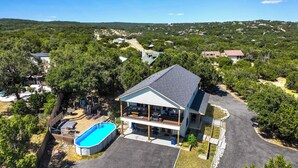 A two-story house with a swimming pool, surrounded by trees and a hilly landscape. - Scenic Terrace | Private Pool, Hot Tub, Gameroom (Canyon Lake)
