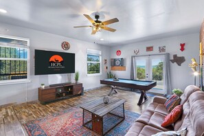 Een woonkamer met een pooltafel, een bank, een televisie en een plafondventilator.