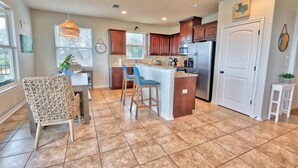 A kitchen with wooden cabinets, a central island with stools, a refrigerator, and a dining area with a chair and table. - Scenic Terrace | Private Pool, Hot Tub, Gameroom (Canyon Lake)