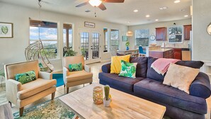 A spacious living room with a dark blue sofa, two armchairs, and a wooden coffee table. There is a hanging chair, a large window, and a view of the outdoors. - Scenic Terrace | Private Pool, Hot Tub, Gameroom (Canyon Lake)
