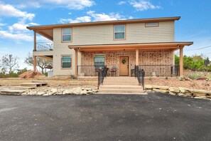 A two-story house with a front porch, a stone retaining wall, and a clear sky. - Scenic Terrace | Private Pool, Hot Tub, Gameroom (Canyon Lake)