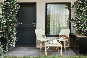 A black door with the number 103, two wicker chairs with a table and a teapot, and a window with a curtain. - Hôtel Botaniste (Paris)