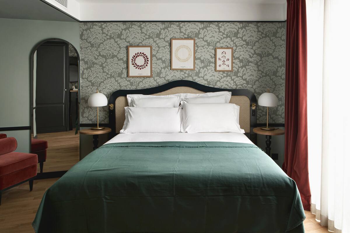 A neatly arranged bedroom with a bed, two bedside tables, a red chair, and a door.