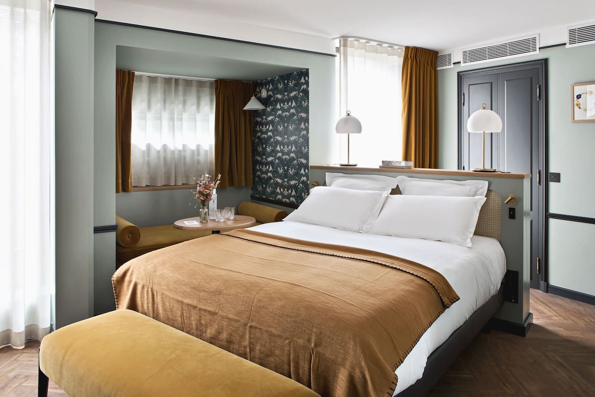 A hotel room with a large bed, a bedside table, a chair, a desk, and a wardrobe.