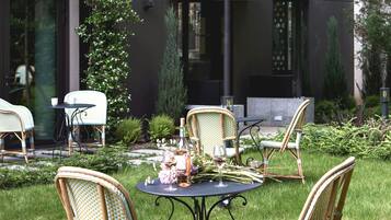Un espace extérieur aménagé avec des chaises et une table en osier, entouré de verdure et avec un bâtiment moderne en arrière-plan.