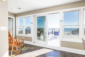Una habitación con vista al océano, una puerta corrediza de vidrio y una mecedora de madera.