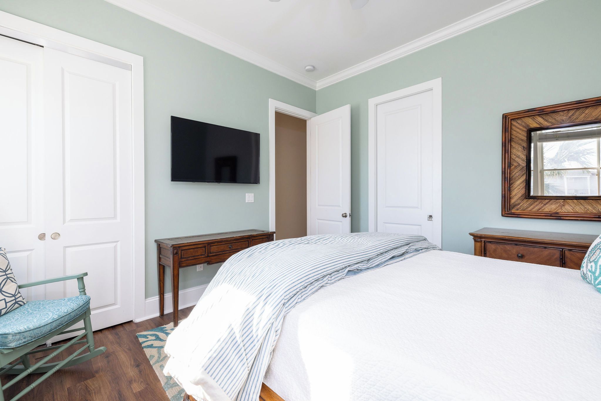 Un dormitorio con cama, escritorio, silla, televisor y una puerta.