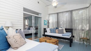 Une chambre à coucher comprenant un lit, un banc, une chaise, une commode en bois et un ventilateur de plafond.