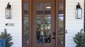 Une porte en bois brun avec un panneau de verre, deux lanternes fixées au mur et une plaque indiquant le numéro de la maison.