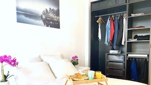 Un lit bien fait, avec un plateau contenant des articles pour le petit-déjeuner, une armoire remplie de vêtements et un tableau encadré accroché au mur.