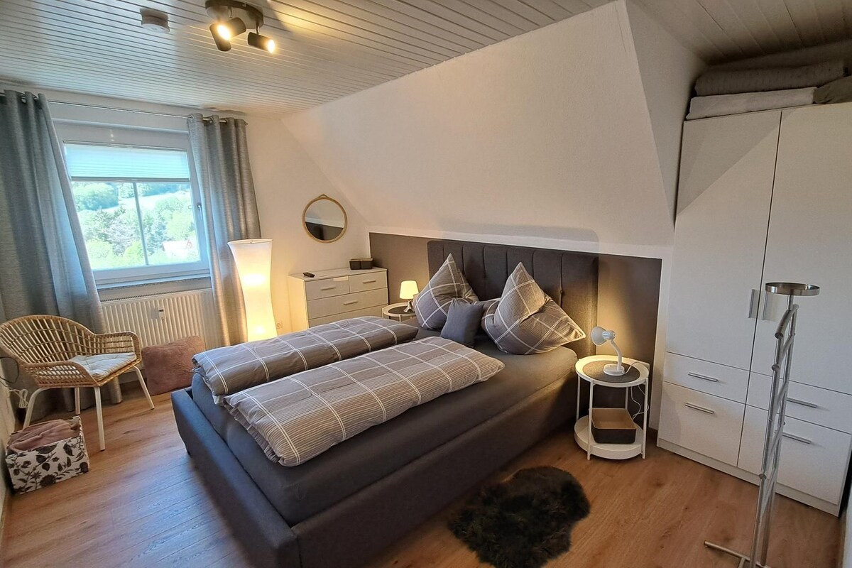 A modern bedroom with a large bed, bedside tables, a wardrobe, and a window with curtains.