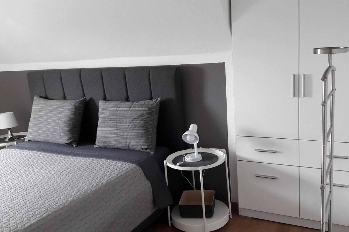 A modern bedroom with a bed, bedside table, lamp, and wardrobe.