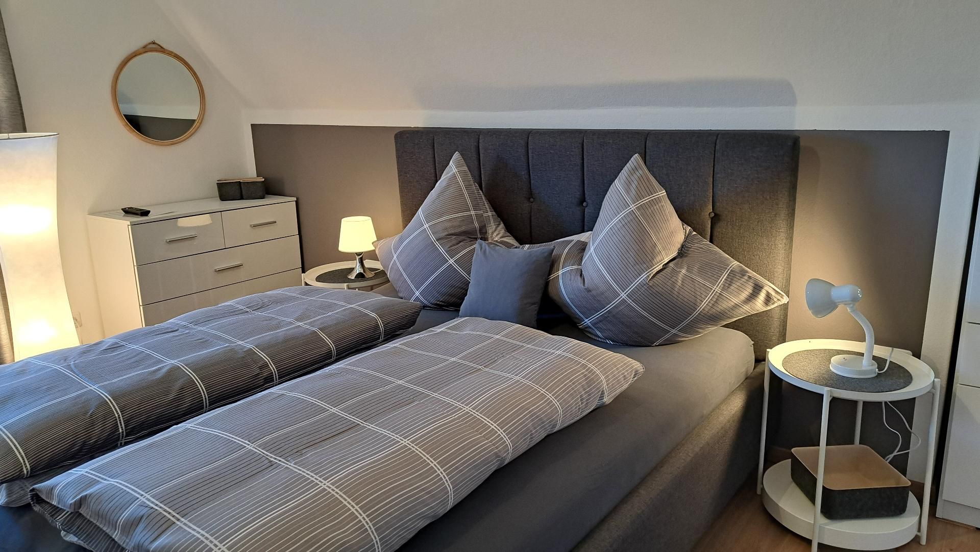 Ein modernes Schlafzimmer mit einem großen Bett, zwei Nachttischen, einer Ablagefläche, einer Lampe und einem Spiegel an der Wand.