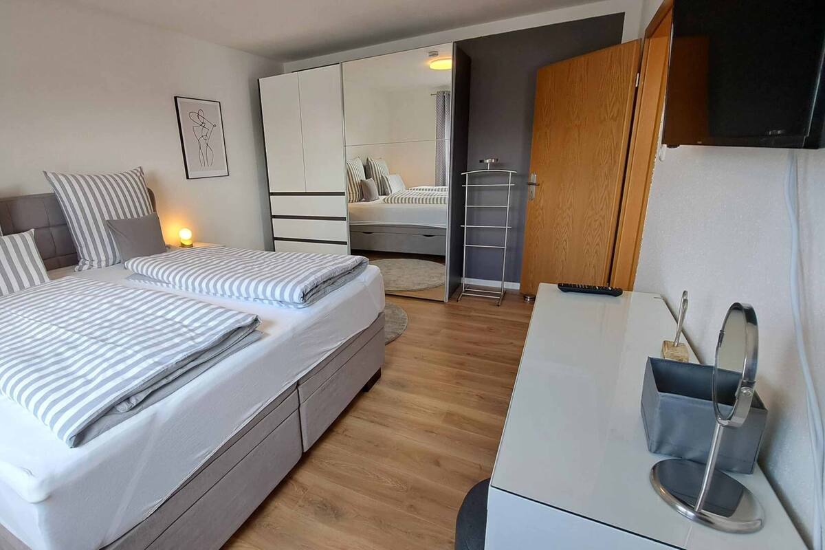 A modern bedroom with a large bed, a desk, and a wardrobe.
