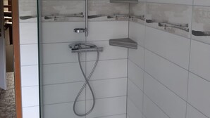 Un espace douche doté d’une porte en verre, d’un pommeau de douche à main et d’une brosse à main.