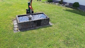 Un bassin rectangulaire avec une pompe, entouré d’une pelouse verdoyante et surmonté, en arrière-plan, d’un bâtiment blanc.