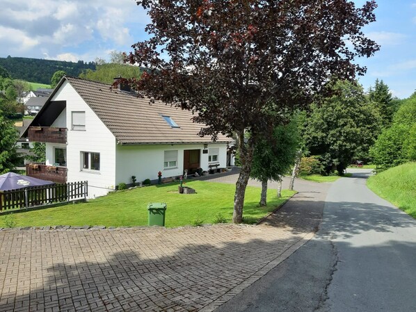 A white house with a tiled roof, a balcony, and a paved driveway.
